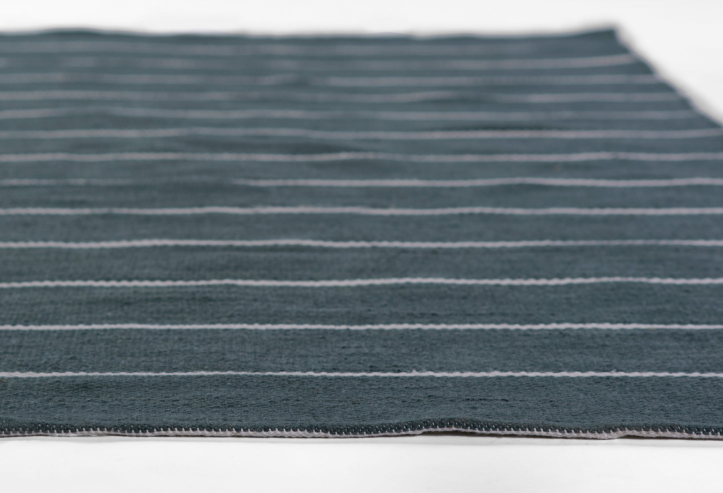 Navy blue striped woven rug with thin white stripes; rectangular floor mat for coastal or modern decor.