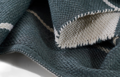 Dark teal woven throw blanket with white stripes, chunky knit texture and white stitched edge.
