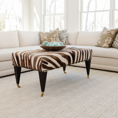 Zebra-print rectangular rug with a turquoise glass bowl on top in a bright living room.