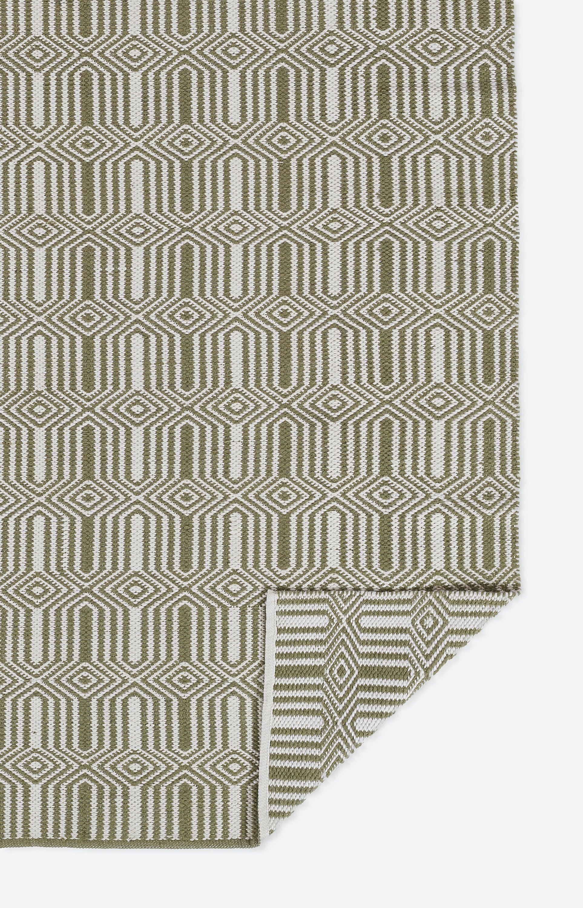 Olive green and cream geometric rug with interlocking diamond shapes; folded corner.