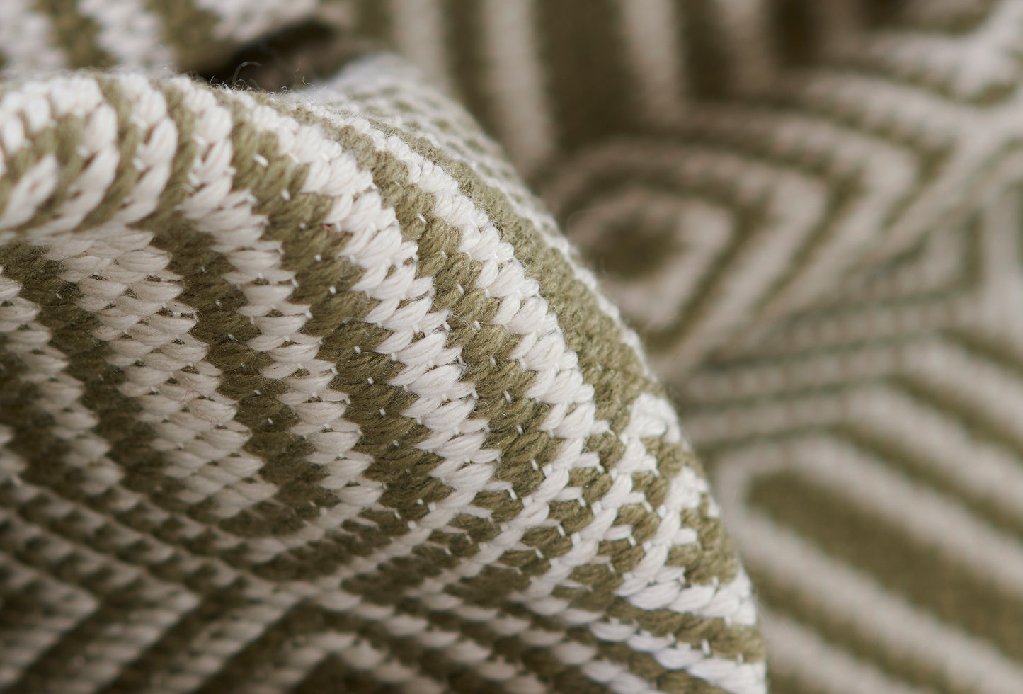 Close-up of olive green and cream woven rug with geometric chevron-like pattern and chunky texture.