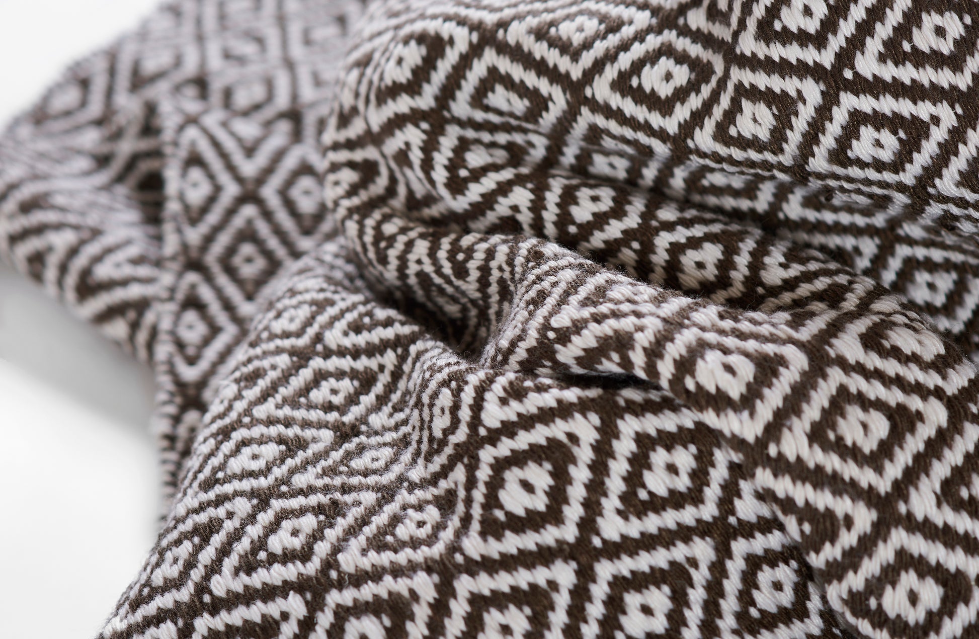 Brown and white diamond-pattern rug with a woven texture, draped in soft folds.