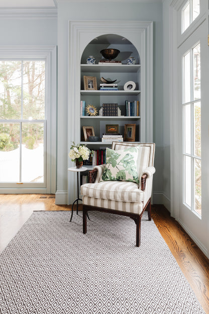 Soft blue geometric rug on the floor in a built-in arched bookcase nook, with a striped armchair, shelves of books, and a green palm cushion.