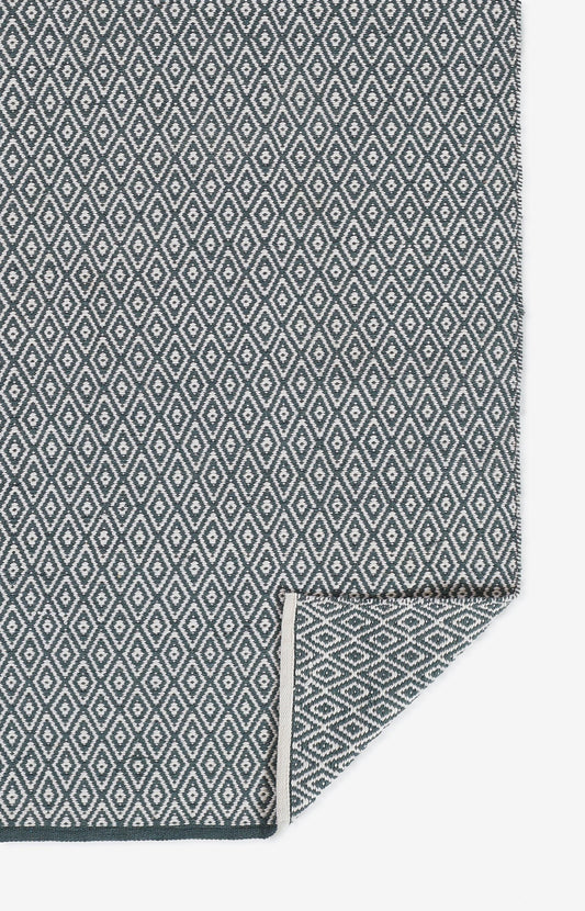 Gray & white diamond lattice woven rug with fringed edge and folded corner.