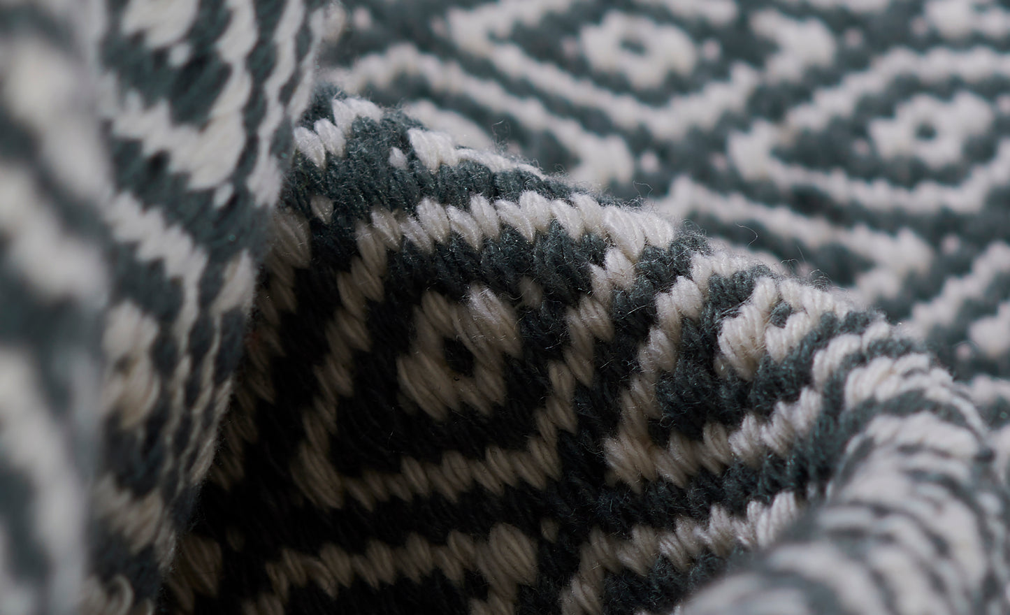 Close-up of teal and ivory geometric knit blanket with chunky woven texture and folded edge.