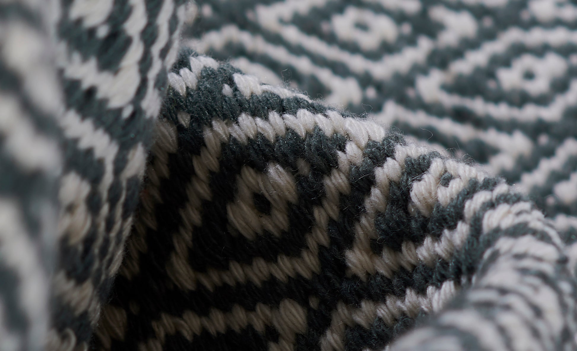 Close-up of teal and ivory geometric knit blanket with chunky woven texture and folded edge.
