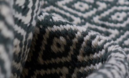Close-up of teal and ivory geometric knit blanket with chunky woven texture and folded edge.