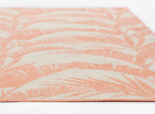 Close-up of coral rug with cream fern-like tropical leaf pattern and visible edge.