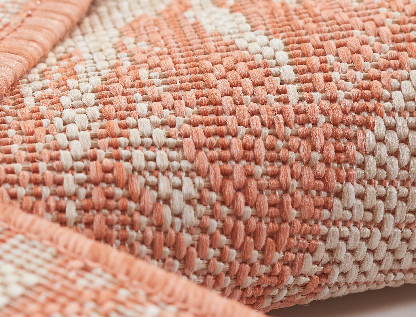 Close-up of coral and ivory woven textile with chunky yarns and textured surface, rug.