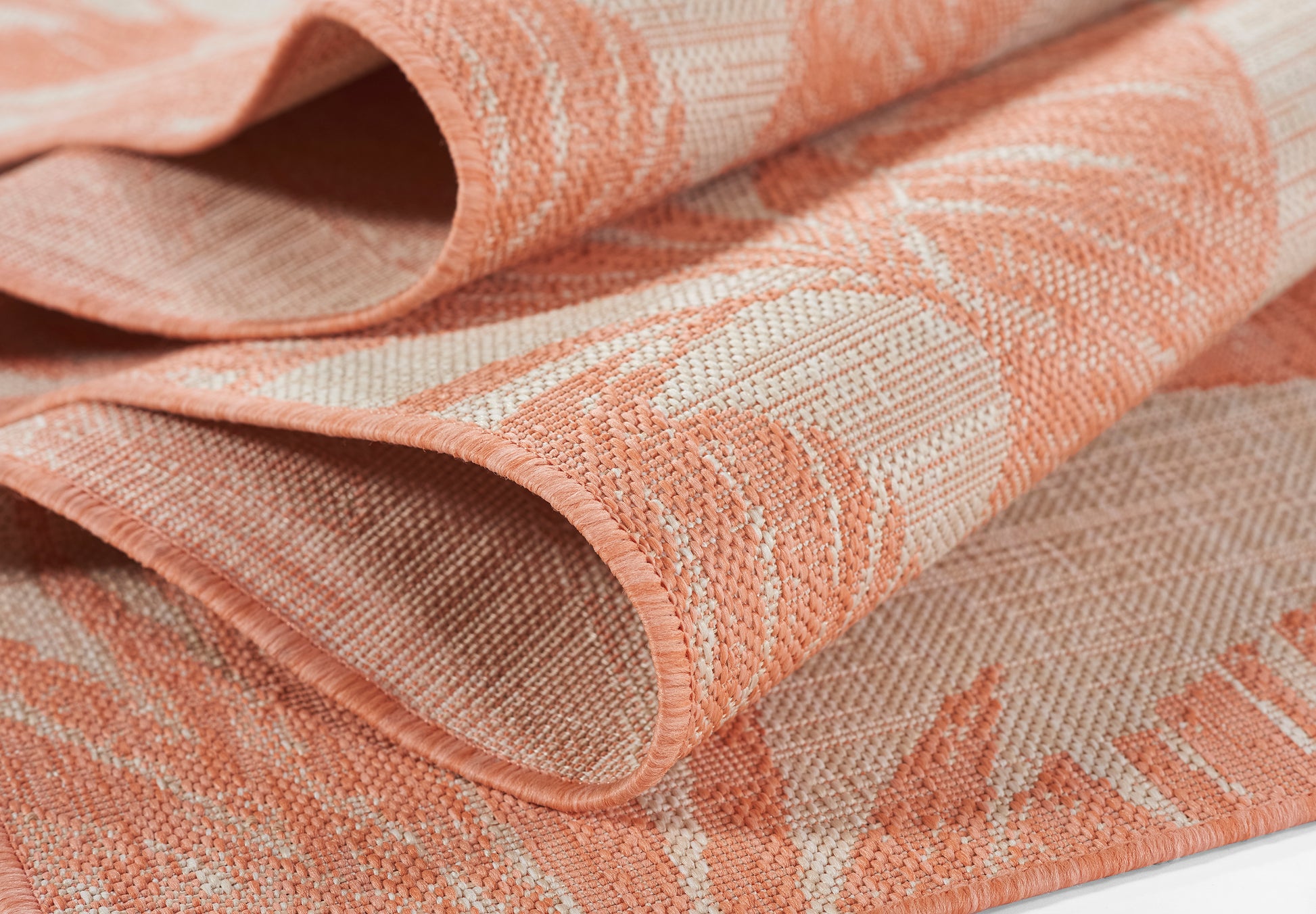 Peach and coral woven fabric with a subtle leaf pattern, folded to show texture; ideal for upholstery or home décor.