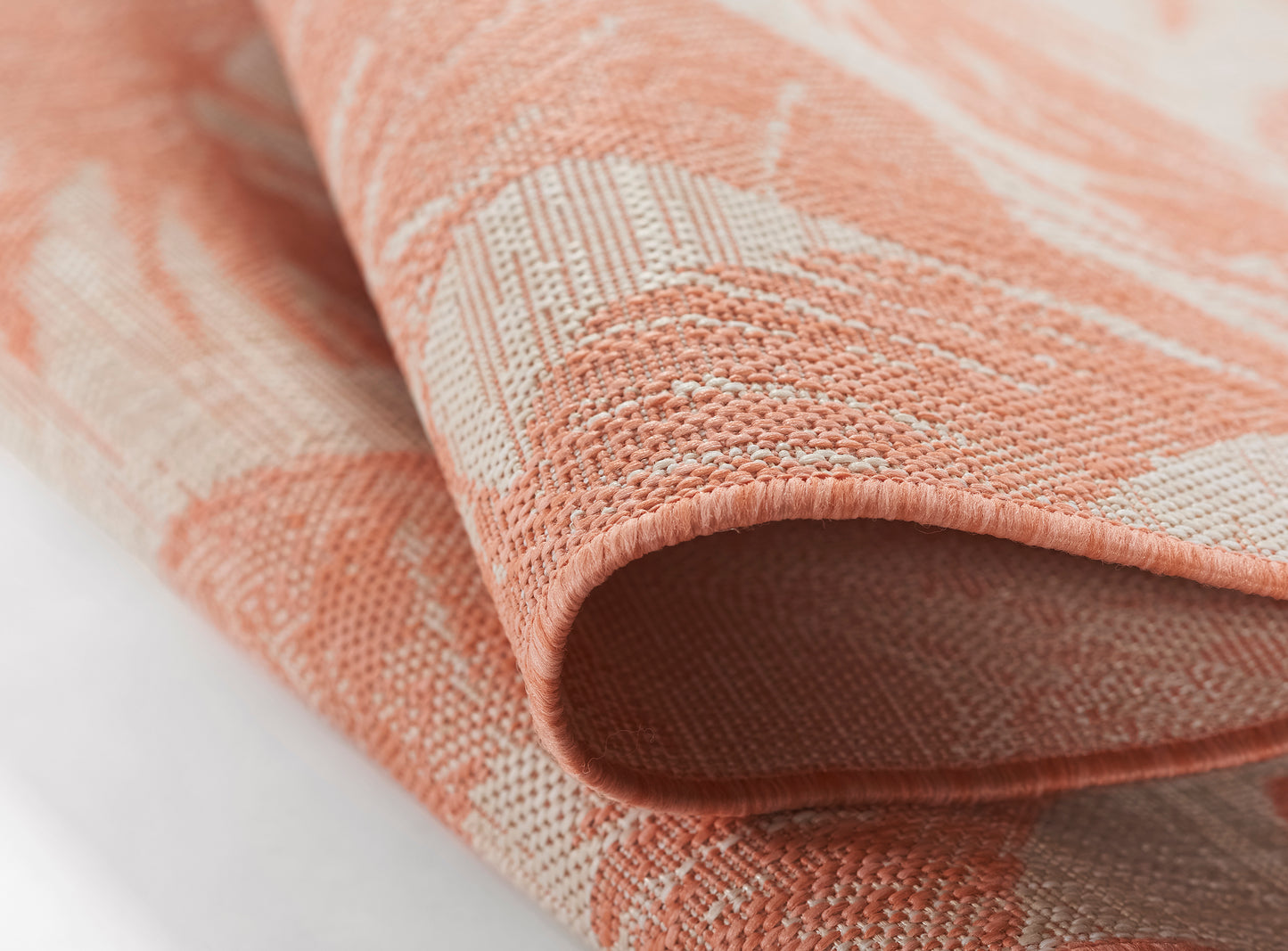 Close-up of coral-pink woven fabric with white geometric pattern and folded edge.