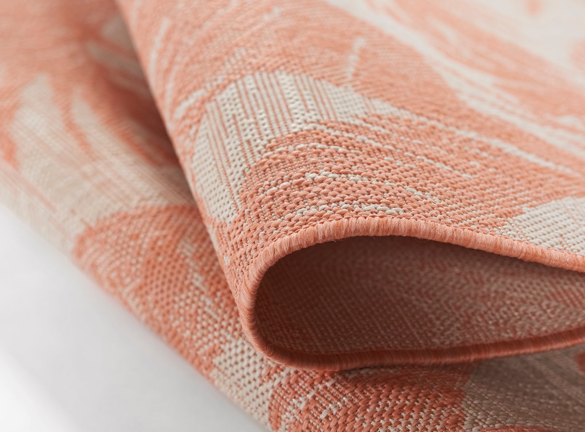 Close-up of a coral peach rug with a white pattern, folded edge revealing a textured weave.