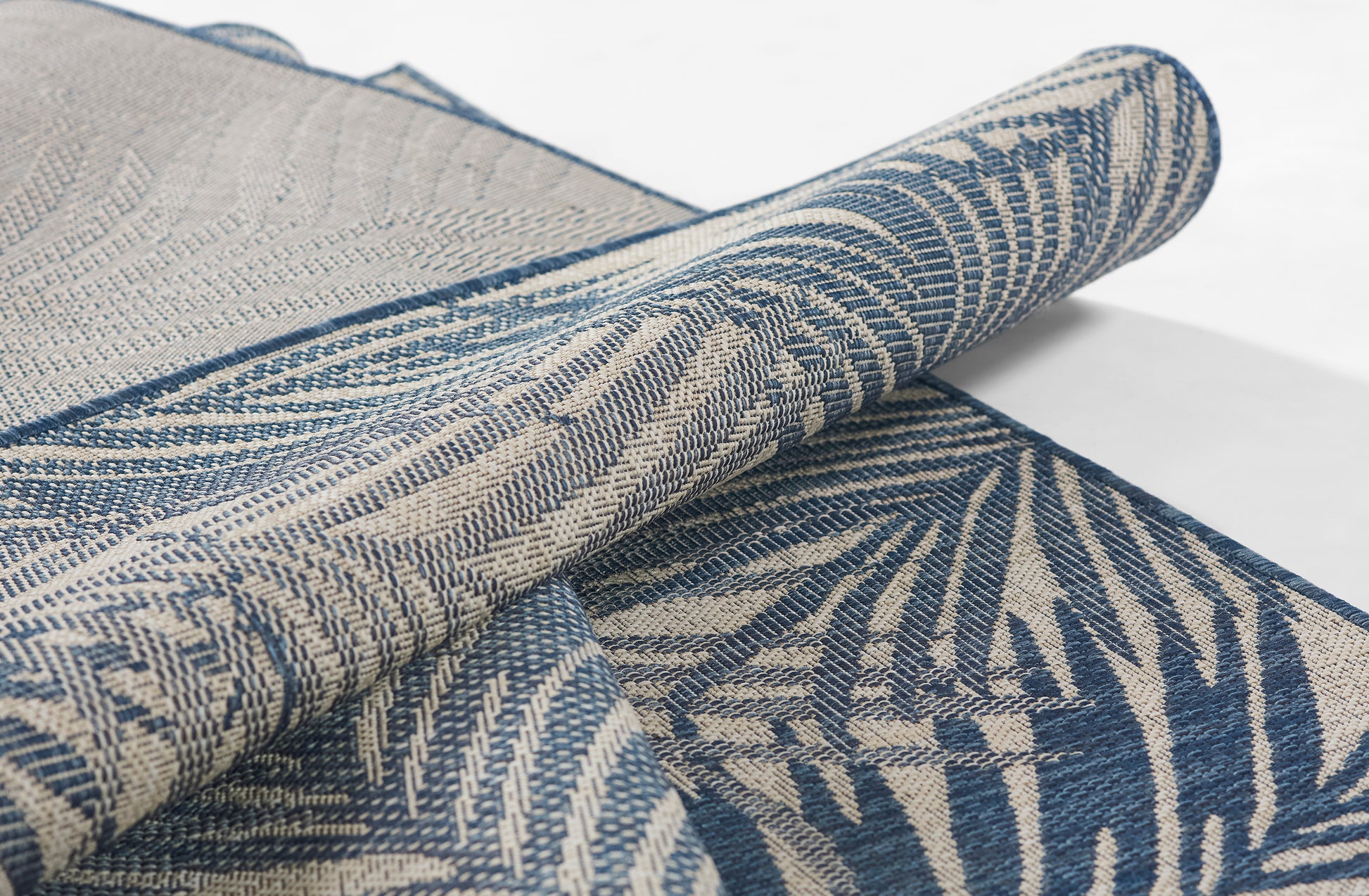 Blue and beige woven textile with palm-leaf pattern, jacquard weave, rolled decorative rug or throw fabric.