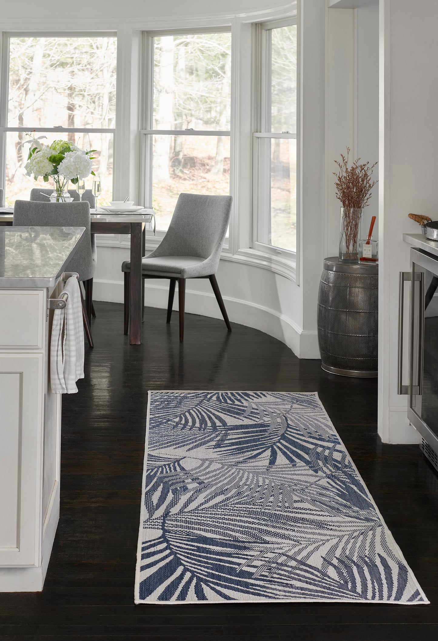 Rectangular blue palm-leaf patterned rug on dark wood floor in a bright white kitchen.