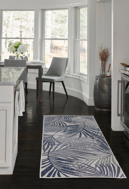 Rectangular blue palm-leaf patterned rug on dark wood floor in a bright white kitchen.
