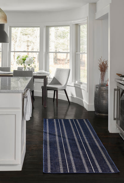 Navy blue rug runner with white geometric stripes on dark wood floor in bright white kitchen and dining nook.