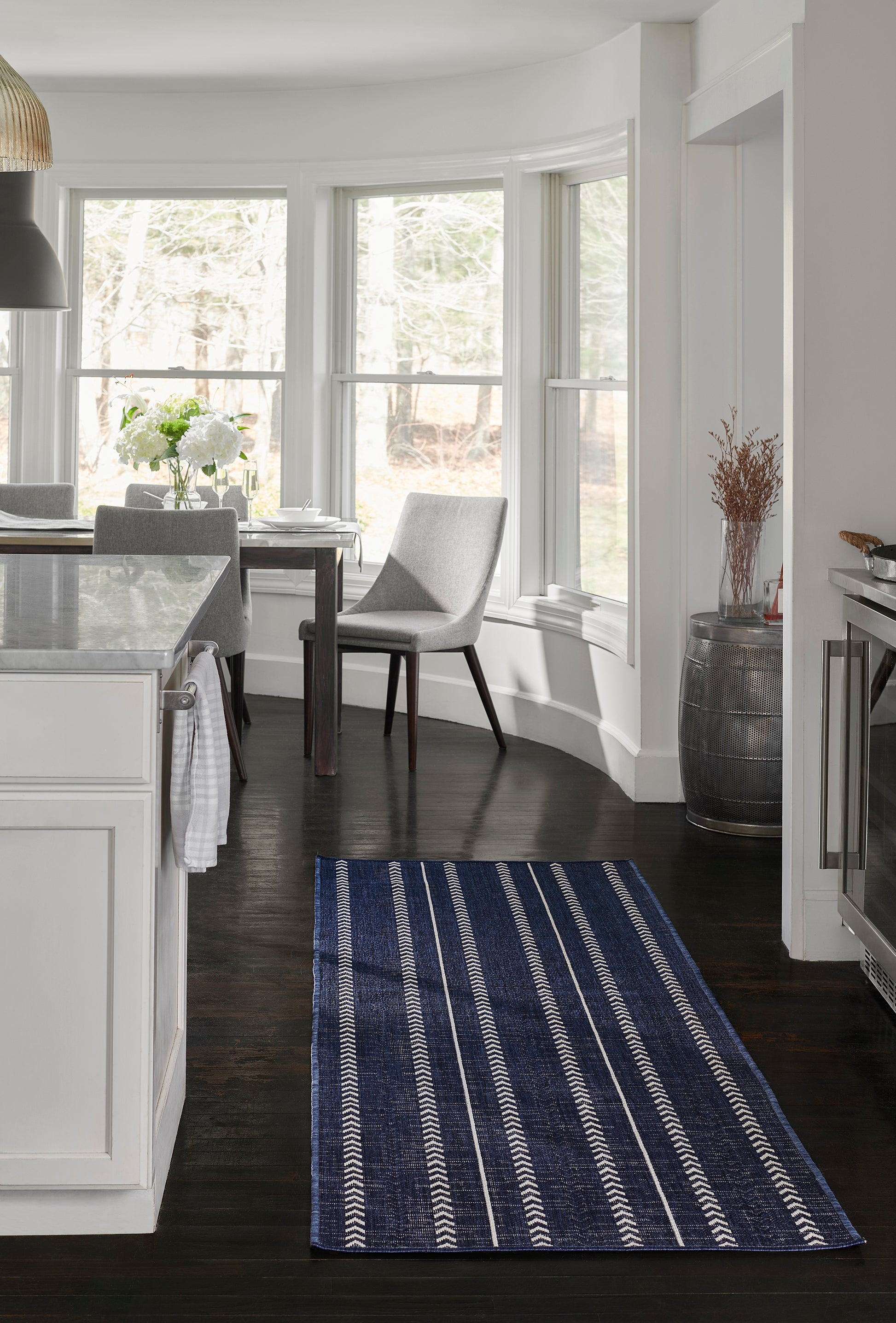Navy striped rug runner in a bright white kitchen with dark wood floor and curved bay windows.