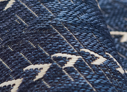 Close-up of indigo denim fabric with white geometric stitching and a textured diagonal weave.