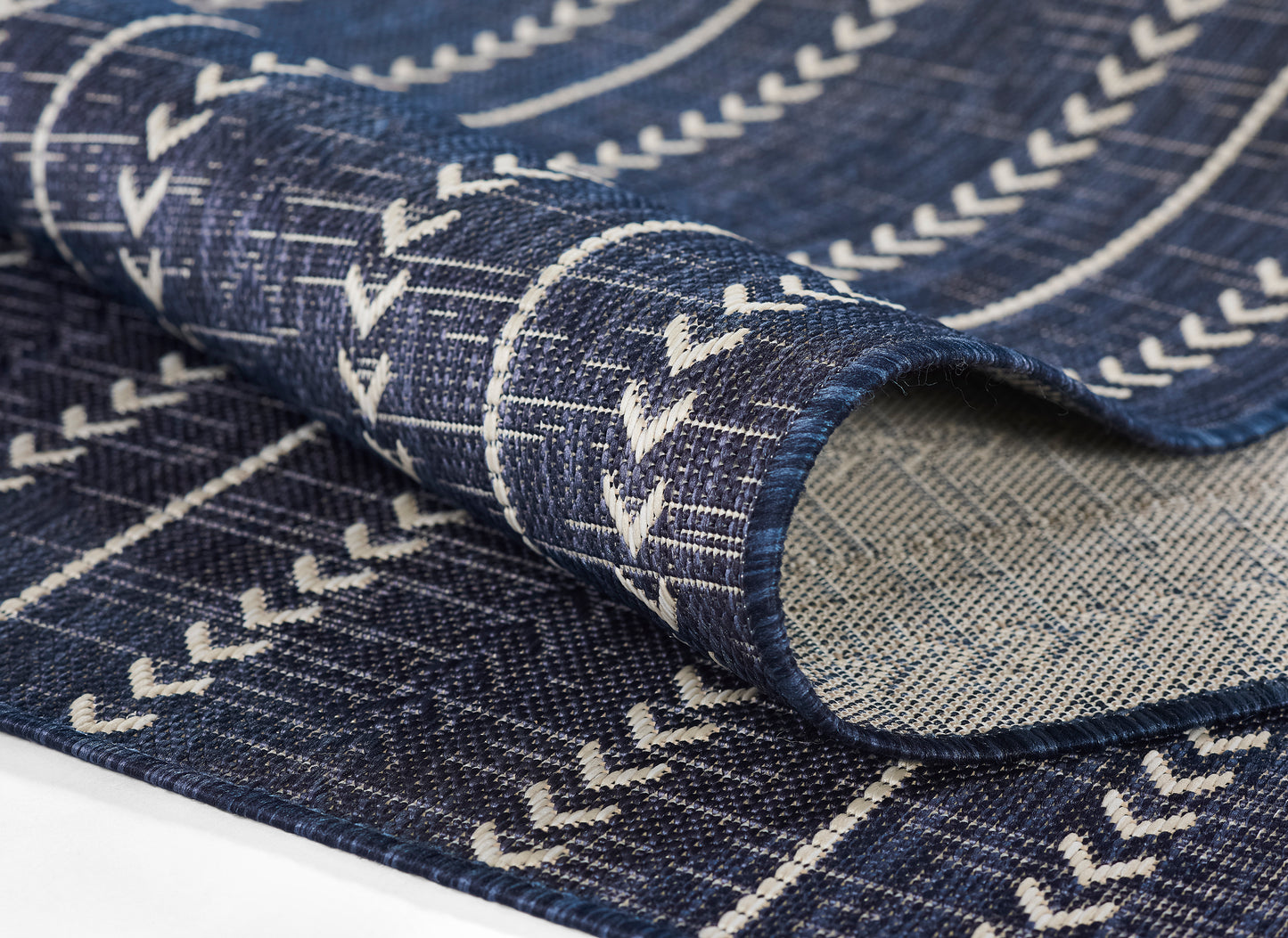 Denim-blue woven rug with white chevron stripes, folded to reveal textured fabric and crisp edges.