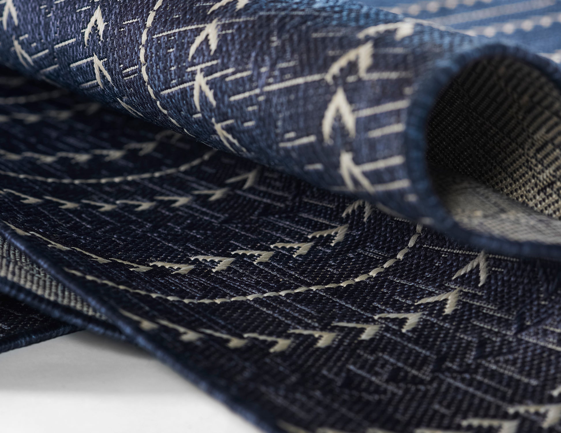 Dark indigo woven fabric with white chevron stitches, folded to show layered edges.