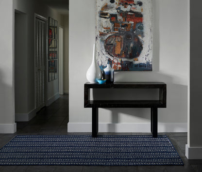 Glossy black lacquer console table under abstract painting with white vases and a blue bowl, navy patterned rug on dark tile.