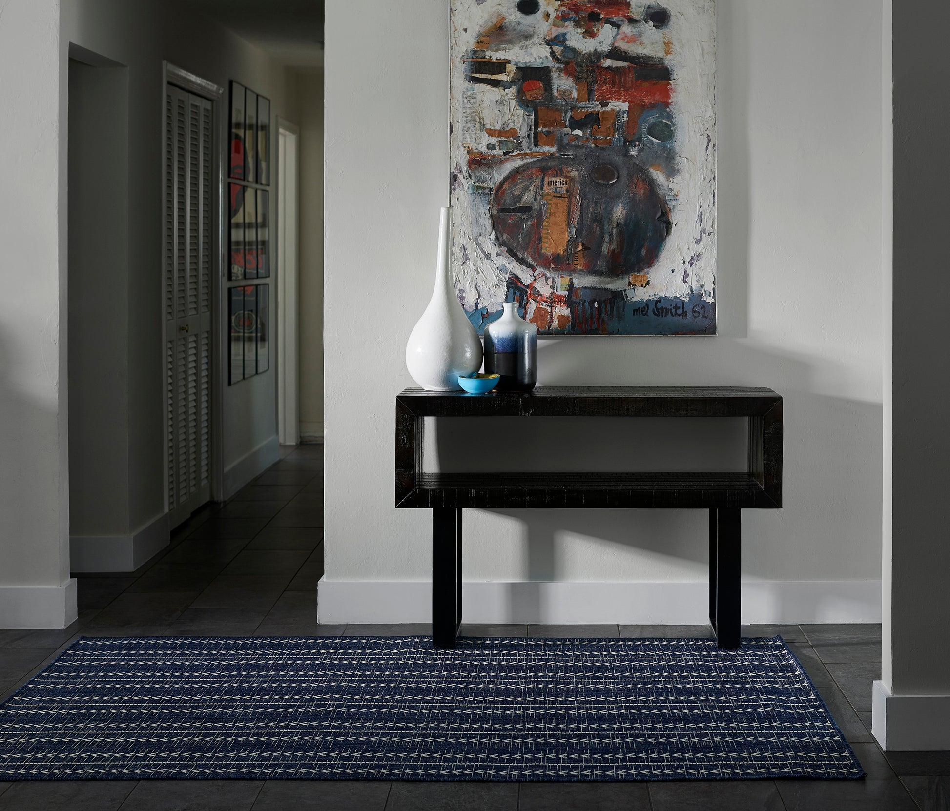 Glossy black console table with white & blue vases and an abstract painting above, set on a blue rug runner in a hallway.