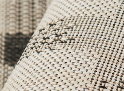Close-up of cream and taupe woven rug texture with dark brown geometric pattern; rustic home decor.