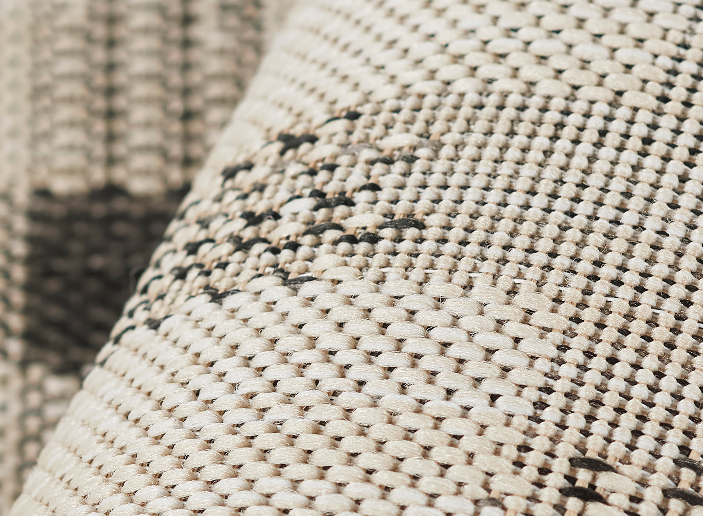 Close-up of beige woven rug with natural fiber texture and dark brown stitched pattern.