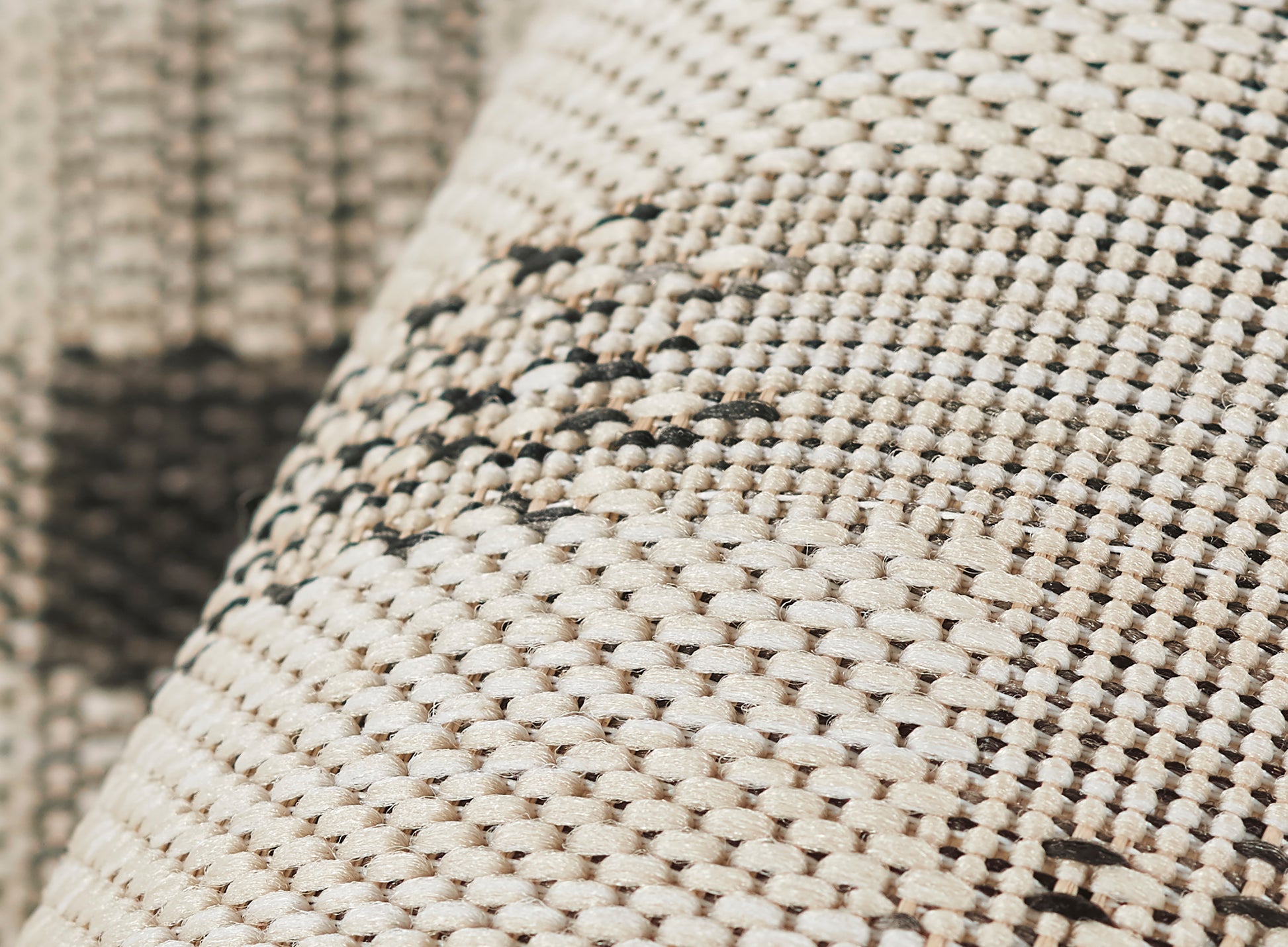 Close-up of beige woven rug with natural fiber texture and dark brown stitched pattern.