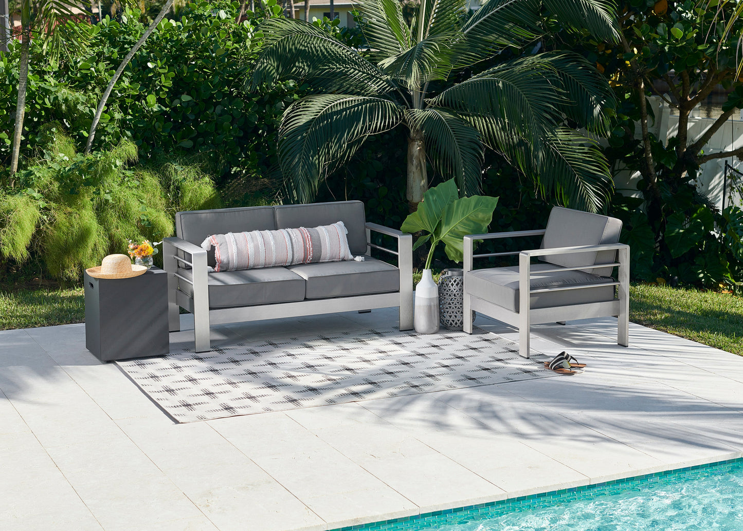 Modern gray outdoor sofa and two armchairs with metal frames, striped pillow, poolside on a light deck with a rug.
