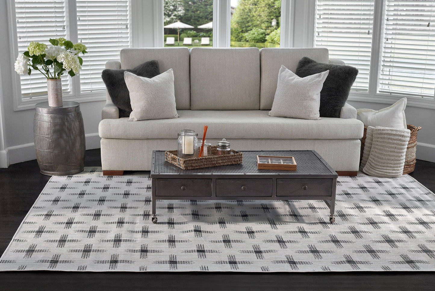 Modern living room with a light gray sofa, white and charcoal pillows, dark wood coffee table, and a gray geometric rug.