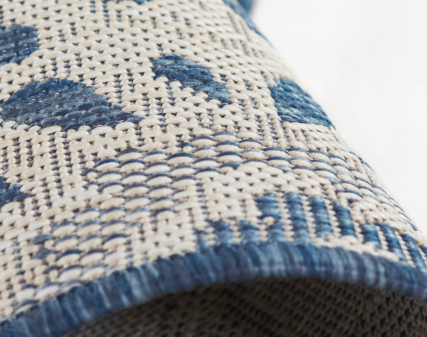 Beige woven rug with blue geometric motifs and blue fringe edge.