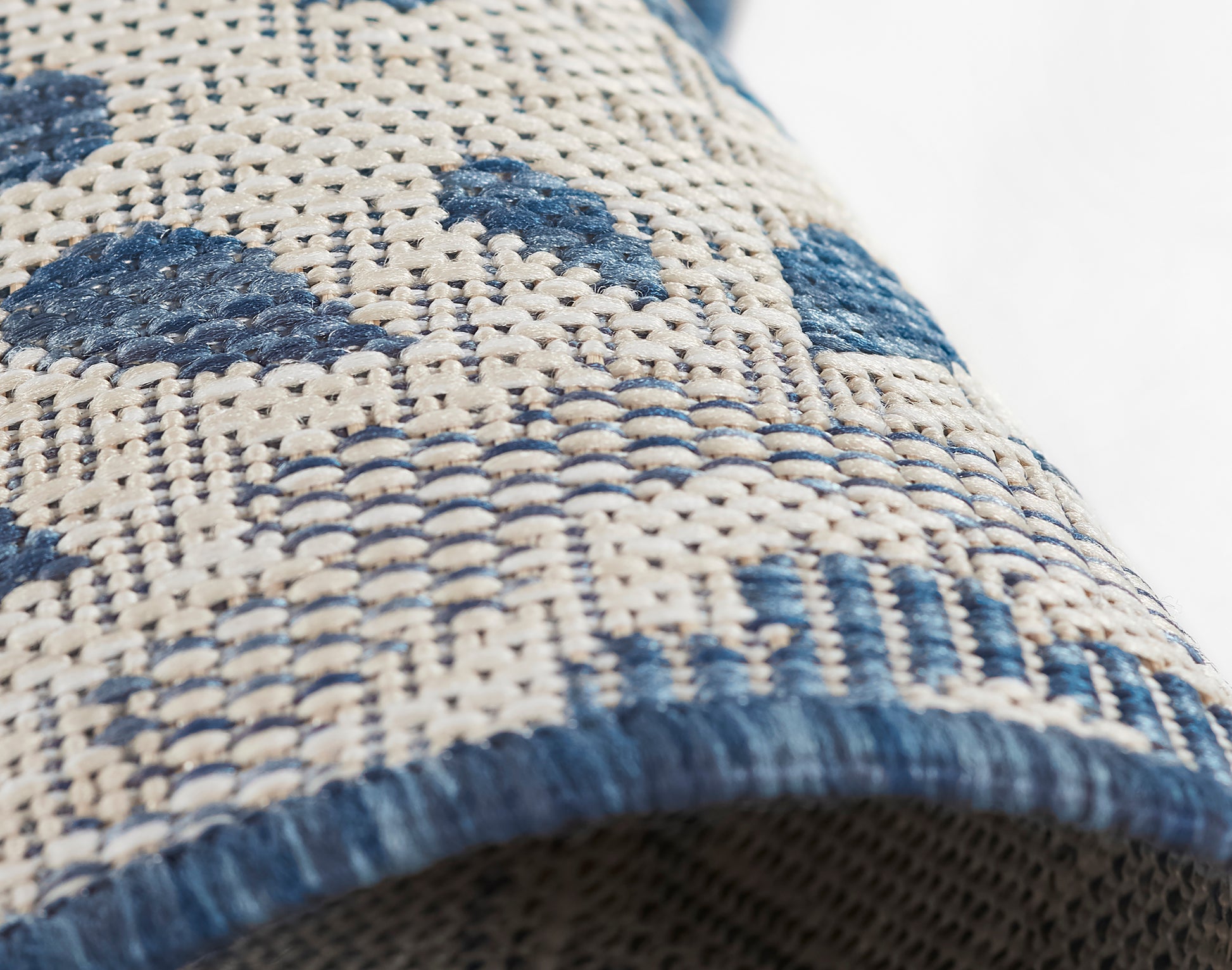 Beige woven rug with blue geometric motifs and blue fringe edge.