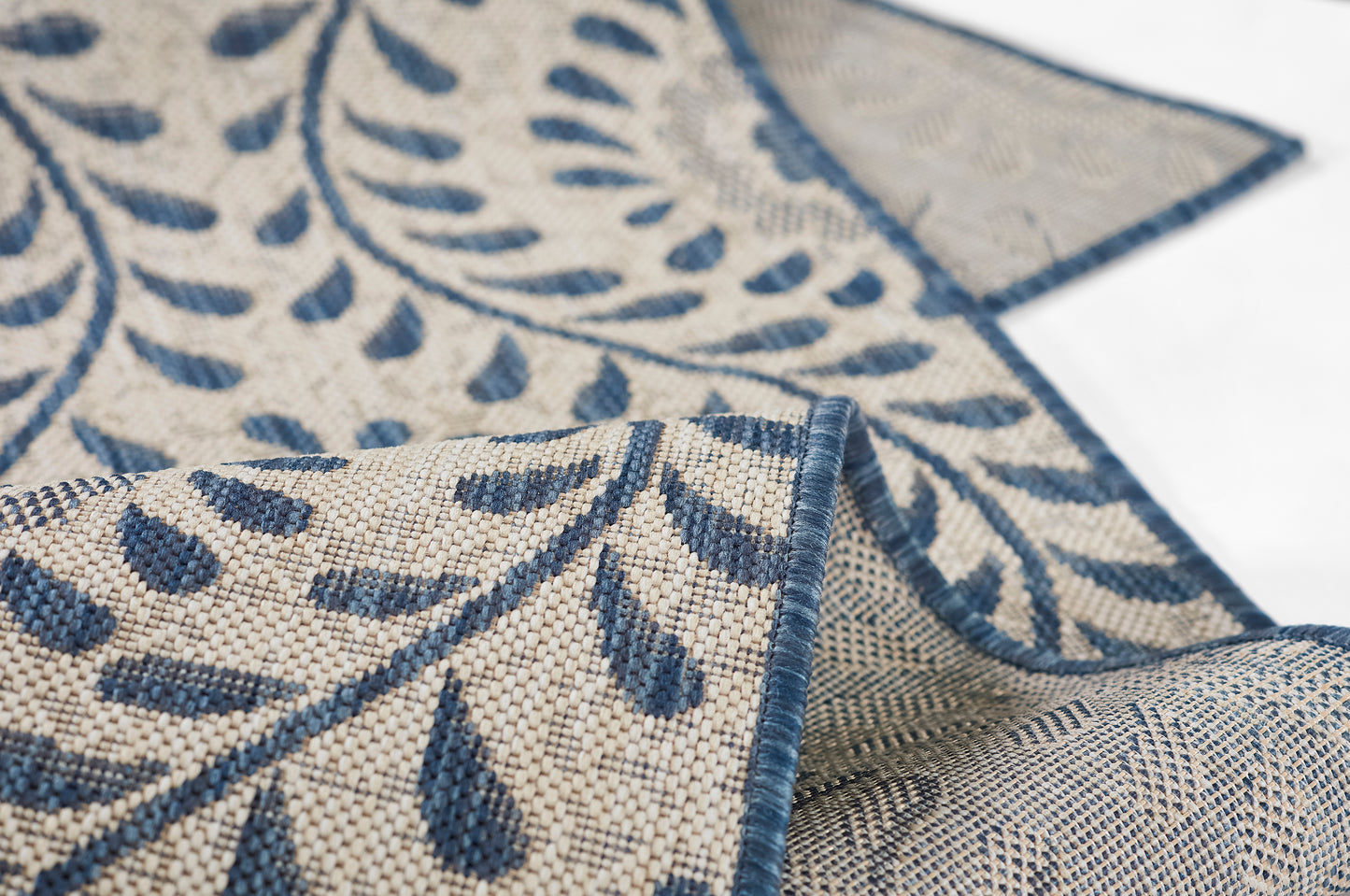 Beige woven fabric with navy blue botanical vine pattern; damask-style textile with blue border, draped.