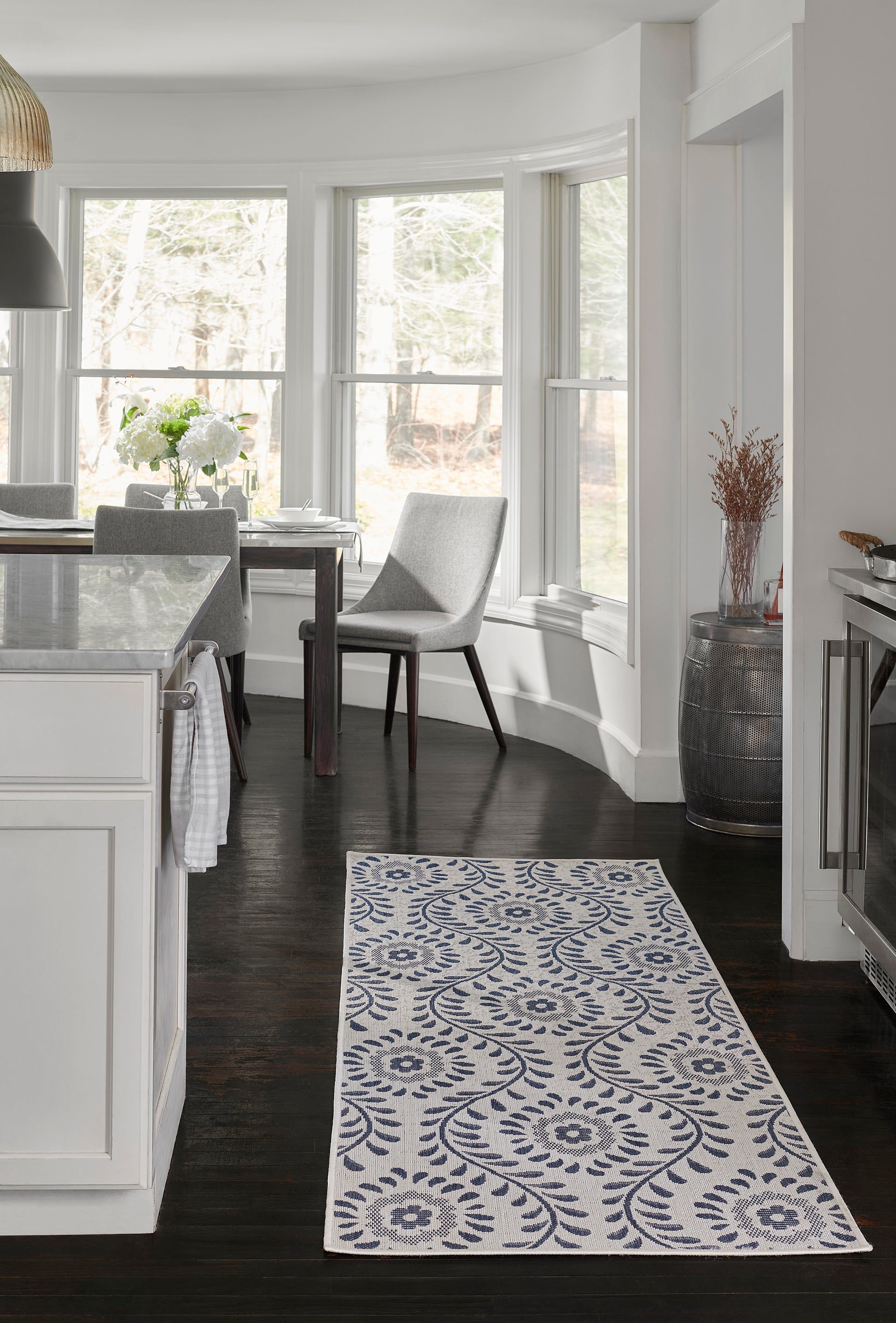 Blue and white patterned rectangular woven runner rug in a modern white kitchen with dark wood floors.