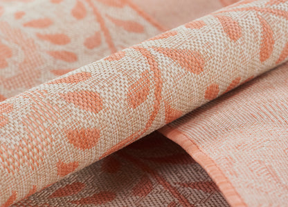 Peach-pink woven rug with coral leaf pattern and rolled edges.