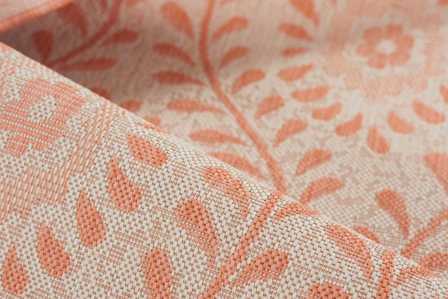 Close-up of coral-pink woven rug with a leaf and floral motif; soft textured surface.