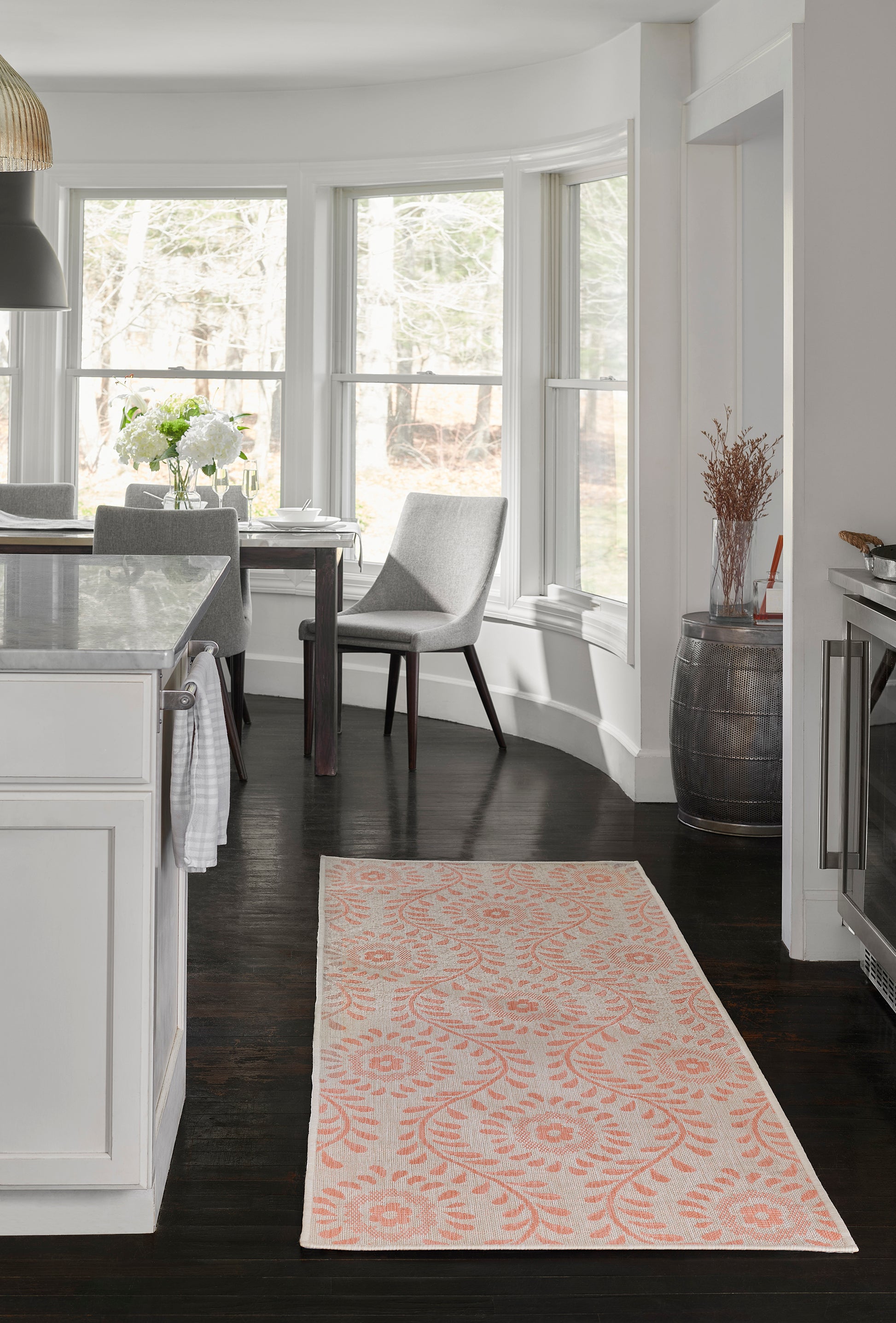 Peach and ivory botanical rug on dark hardwood floor in a bright white kitchen with bay windows.