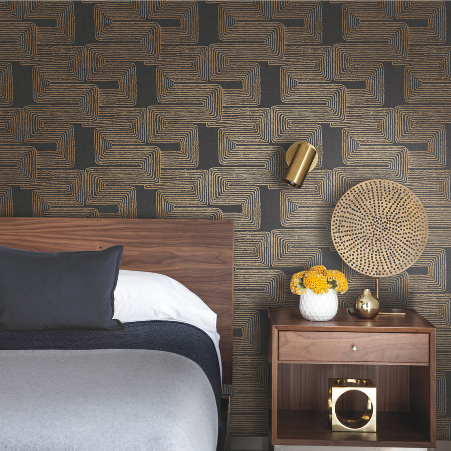 Zulu Signature Peel and Stick Wallpaper by Nikki Chu for RoomMates, featuring a deep neutral background with gold and warm tan organic geometric lines. The layered lines form large interlocking, maze-like rectangular shapes with an irregular woven and hand-crafted appearance. The sophisticated tribal-inspired design adds texture, dimension and an upscale decorative look to statement walls, bedrooms, living rooms, dining rooms, offices and entryways.