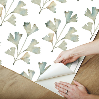 Watercolor blue-green leaf-pattern wallpaper being peeled back by hands