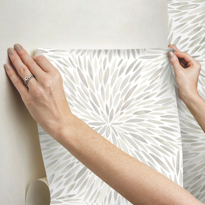 Hands hold a sheet of gray starburst wallpaper; modern geometric print for walls.