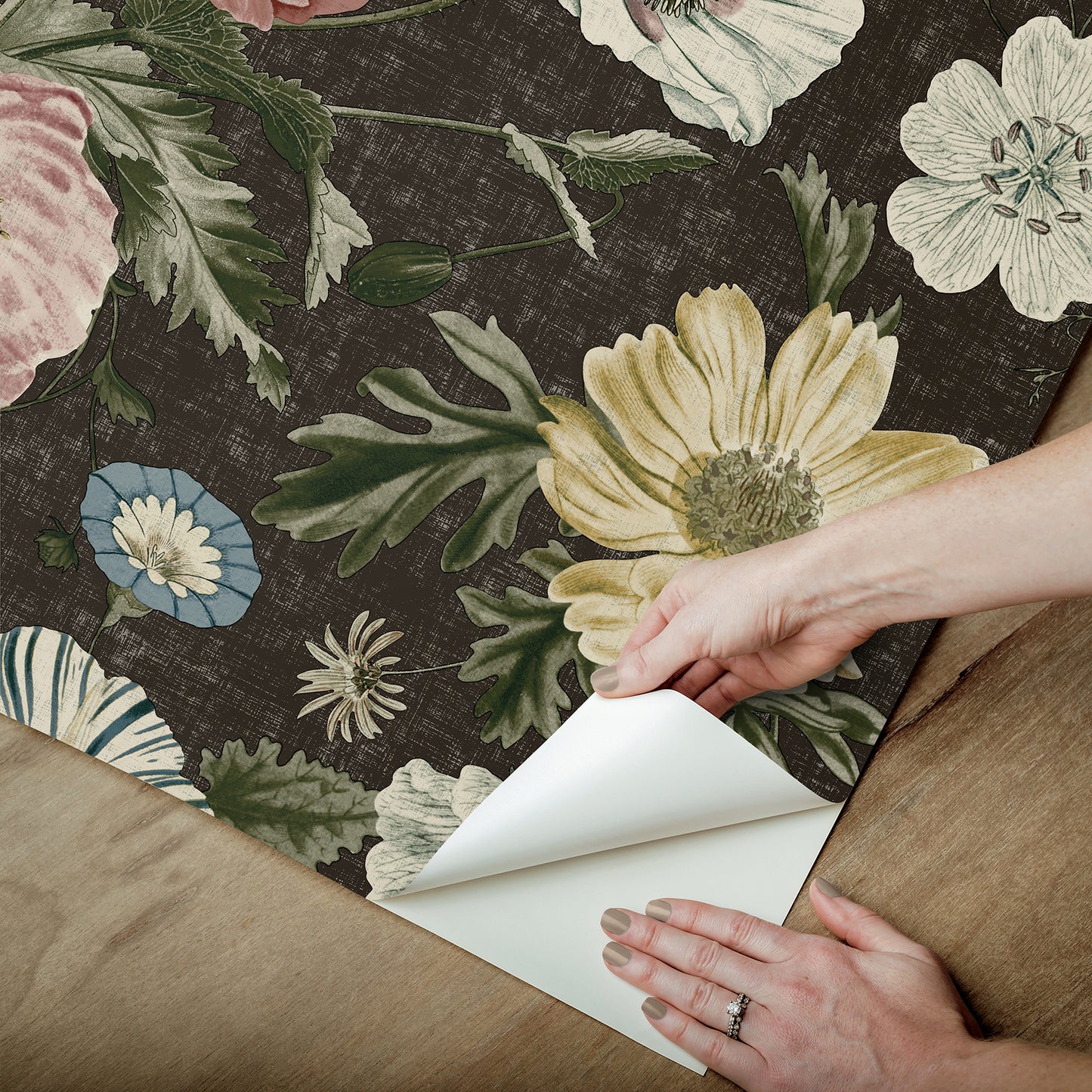 Peel-back corner of dark floral wallpaper featuring large yellow, pink and white flowers with green leaves.