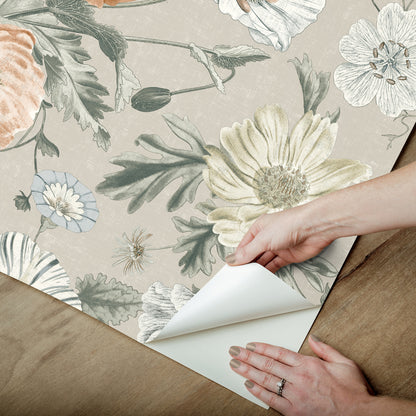 Hand peels floral wallpaper showing pastel beige, peach, and green blooms from wood surface.