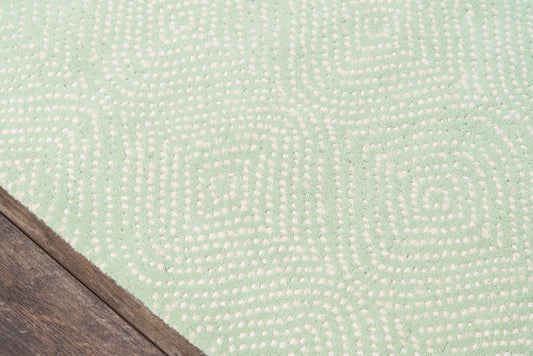 Mint green rug with cream dotted geometric maze pattern; soft texture near wood floor corner.