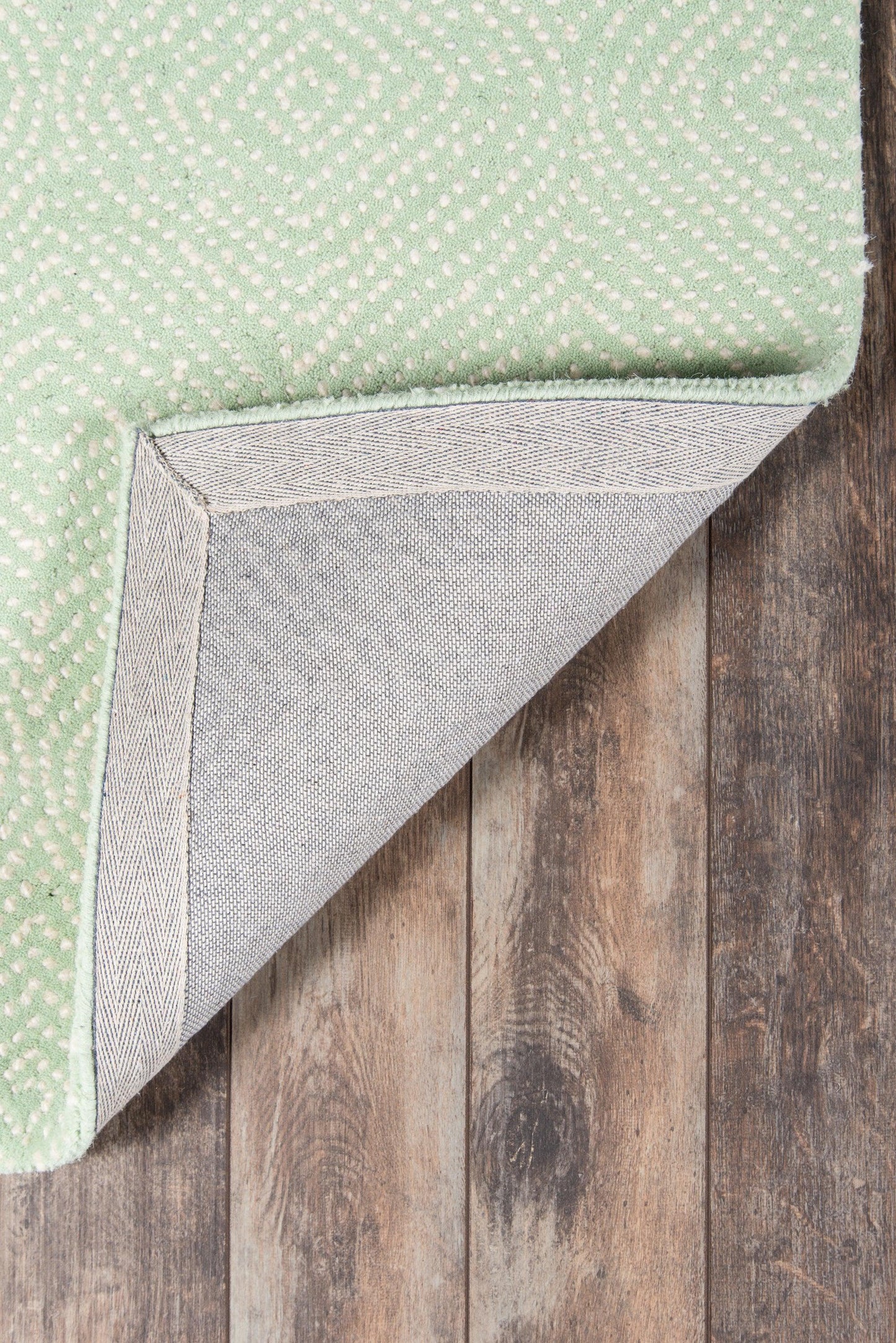 Mint green quilted rug runner with small white dots, folded to reveal light gray underside on a wood floor.
