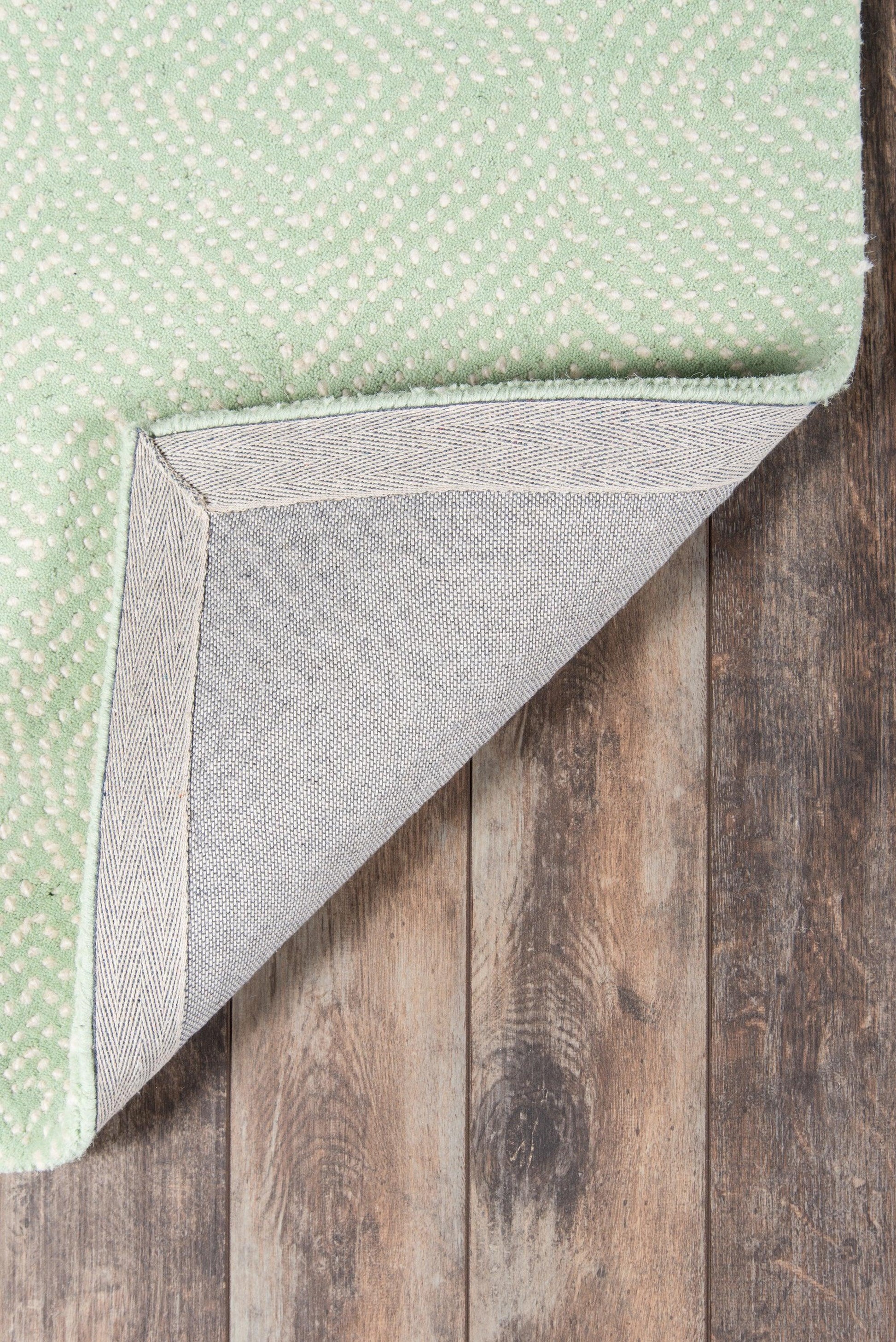 Mint green rug with small white dotted pattern, folded to reveal gray underside on wooden floor.