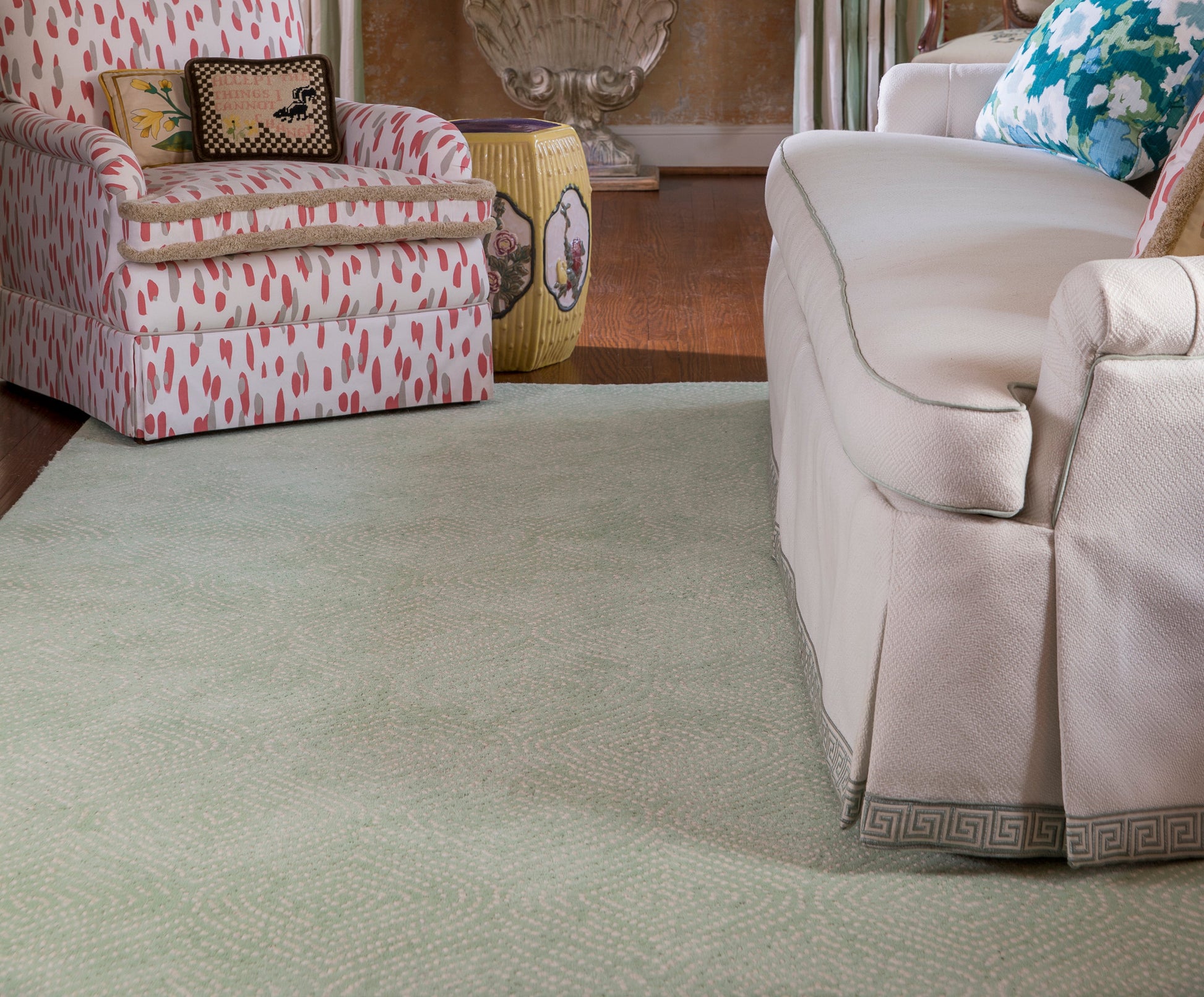 Living room scene with a cream slipcovered sofa (Greek key trim), a pink patterned armchair, a pale green runner rug, and a yellow barrel ottoman.