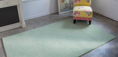 Mint green rectangular woven area rug in a bright living room with a floral yellow chair and white desk.