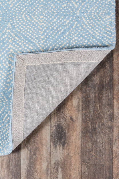 Light blue rug with white dotted pattern, folded corner reveals gray woven backing on dark wood floor.