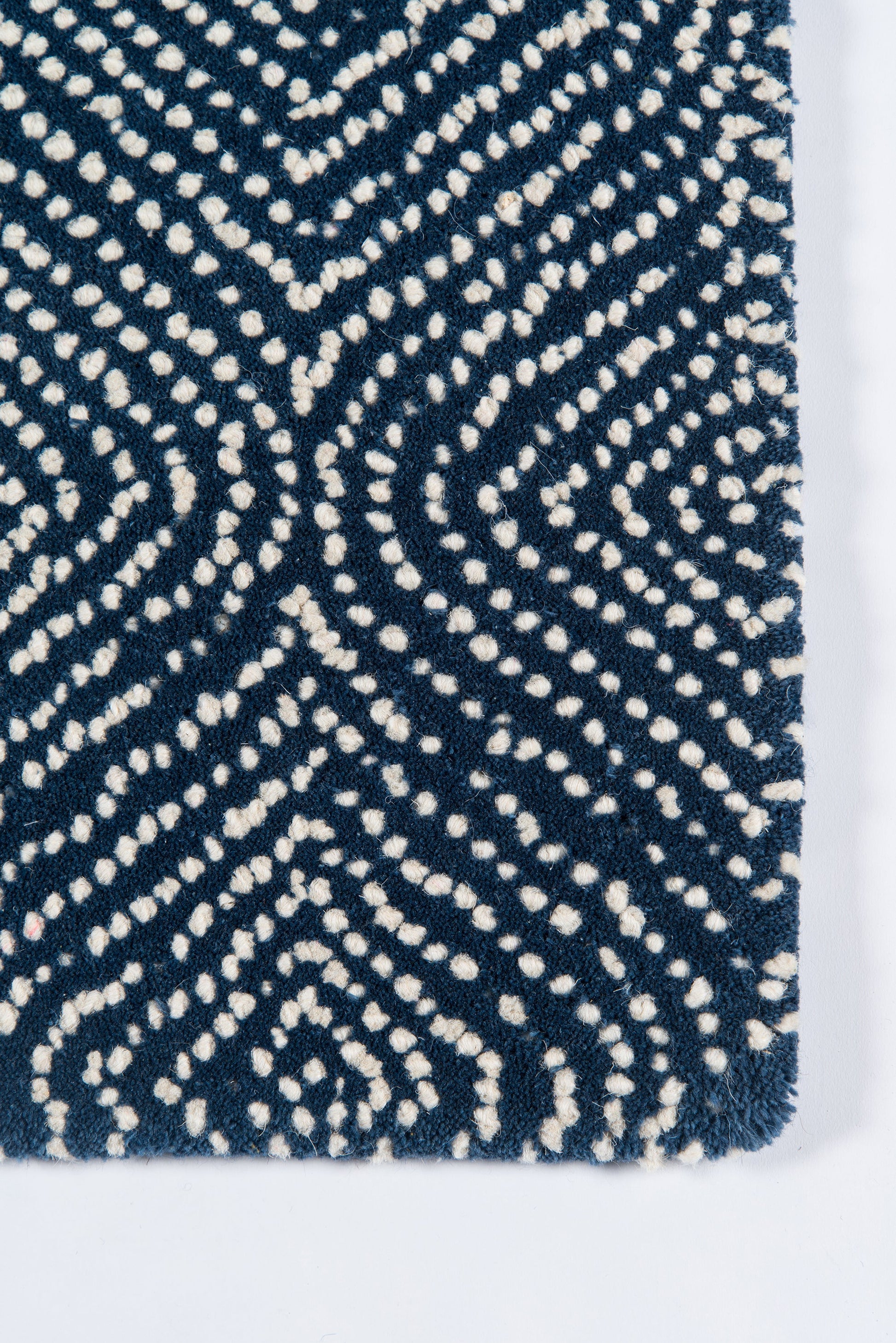 Navy blue tufted rug with ivory dotted geometric swirl pattern; loop pile for modern decor.
